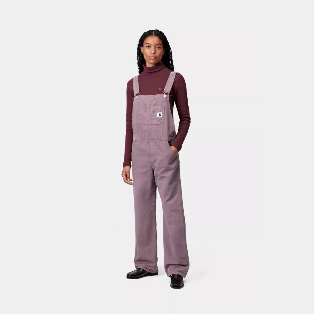 Salopette Carhartt WIP Bib Overall Straight femme en toile Hubbard 100 % coton 9 oz, coupe droite avec poches multiples et Square Label – dispo à Mons. Porté par un mannequin