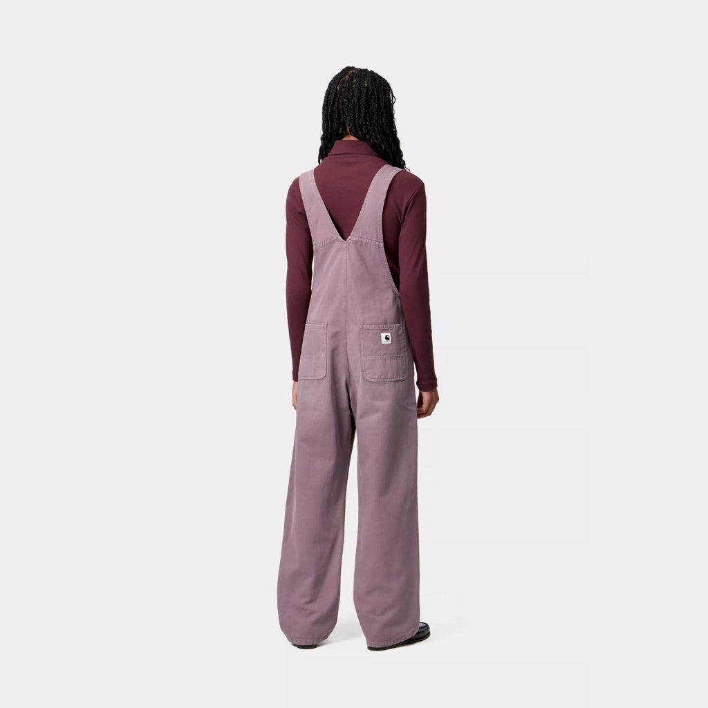 Salopette Carhartt WIP Bib Overall Straight femme en toile Hubbard 100 % coton 9 oz, coupe droite avec poches multiples et Square Label – dispo à Mons. Porté par un mannequin vu de dos