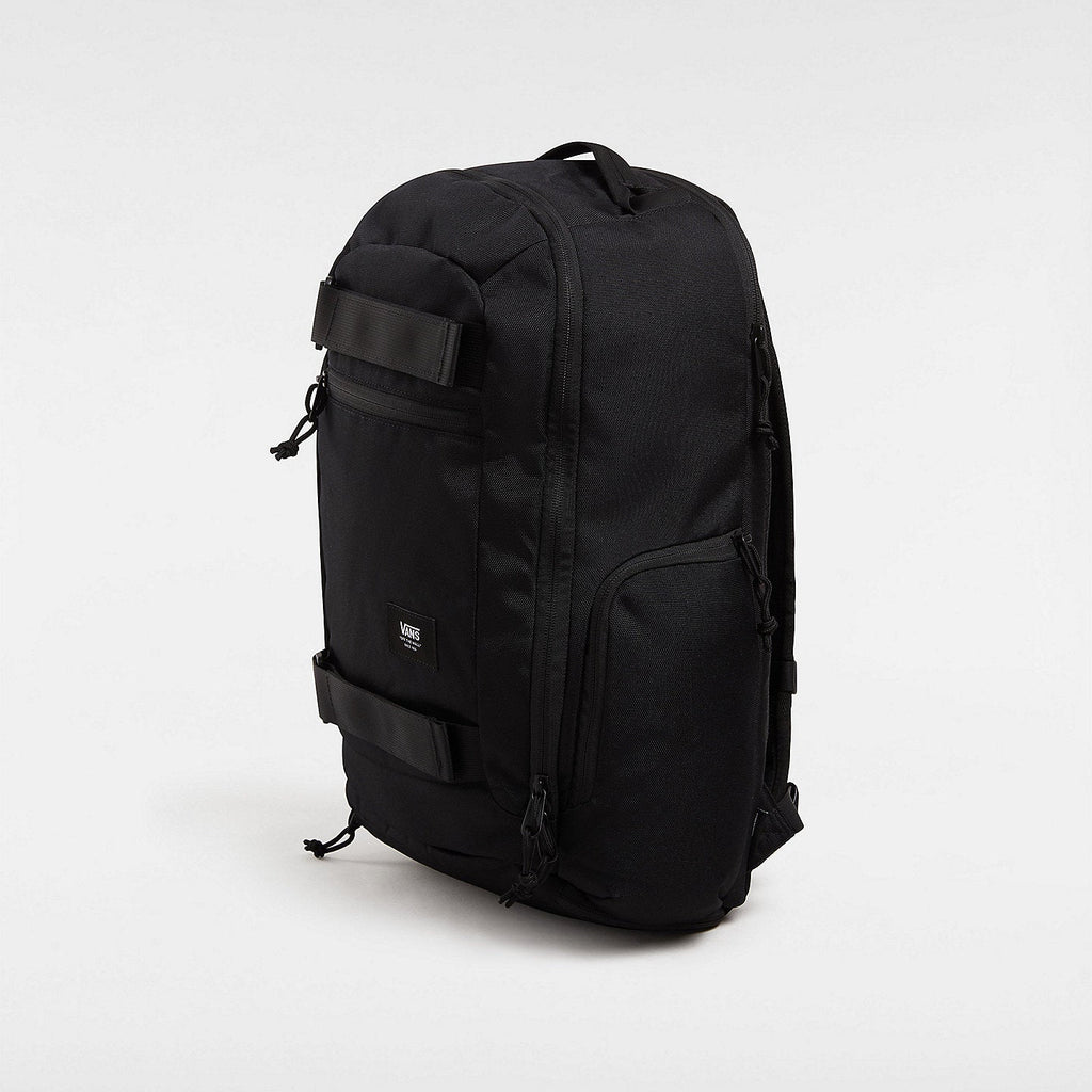 Vue 3/4 du sac à dos Vans DX Skate Noir, mettant en évidence ses attaches réglables pour skateboard et sa poche latérale extensible.